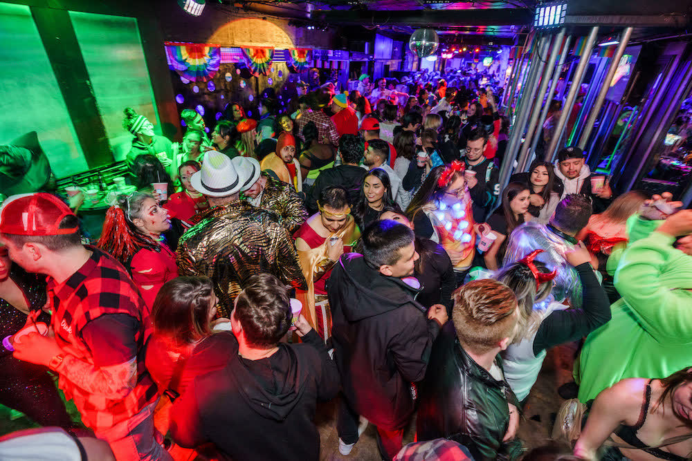 A packed downtown Reno bar full of costumed crawlers under colored party lights