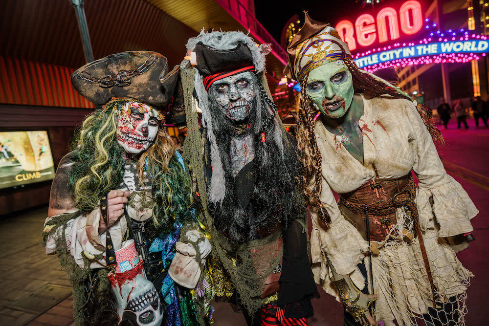 Three crawlers in undead pirate costumes and prosthetic makeup pose downtown with the Reno Arch behind them